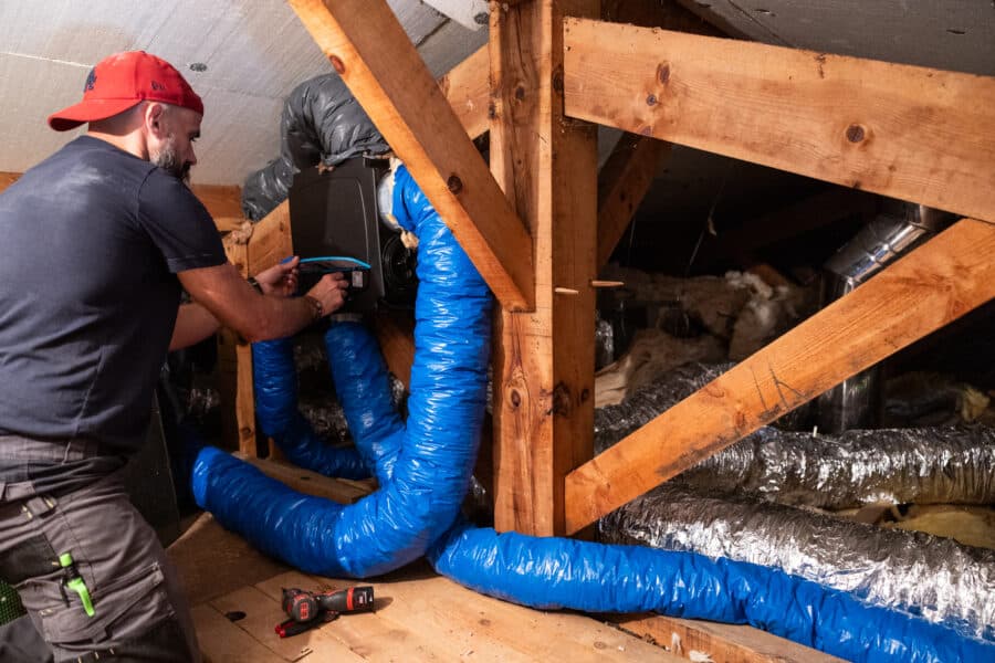 Homme travaillant sur des conduits de ventilation sous toiture.
